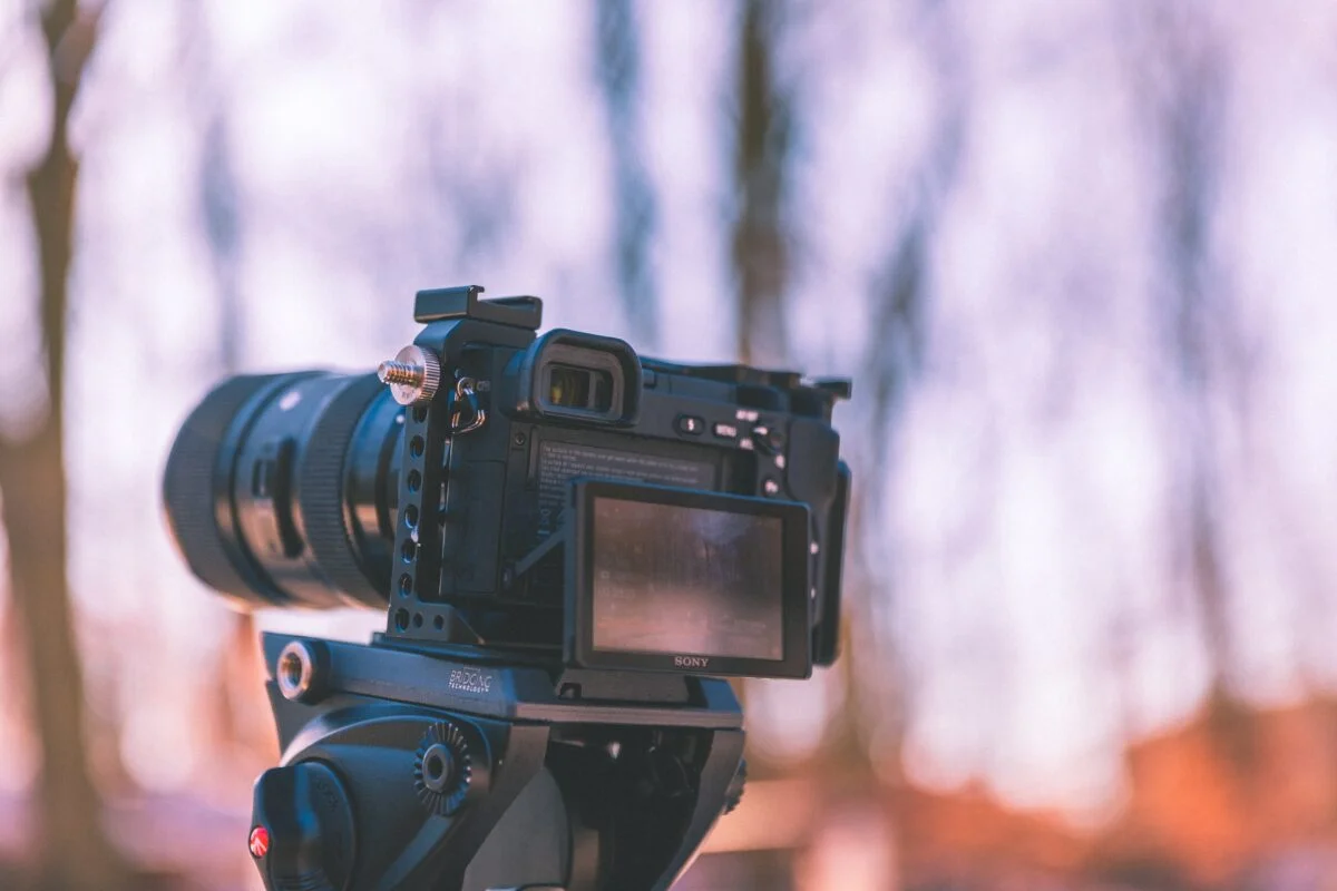 An image of a camera on a tripod focused on a snowy landscape with a vibrant sunrise, highlighting the snow's texture and contrast between deep blue shadows and golden morning light