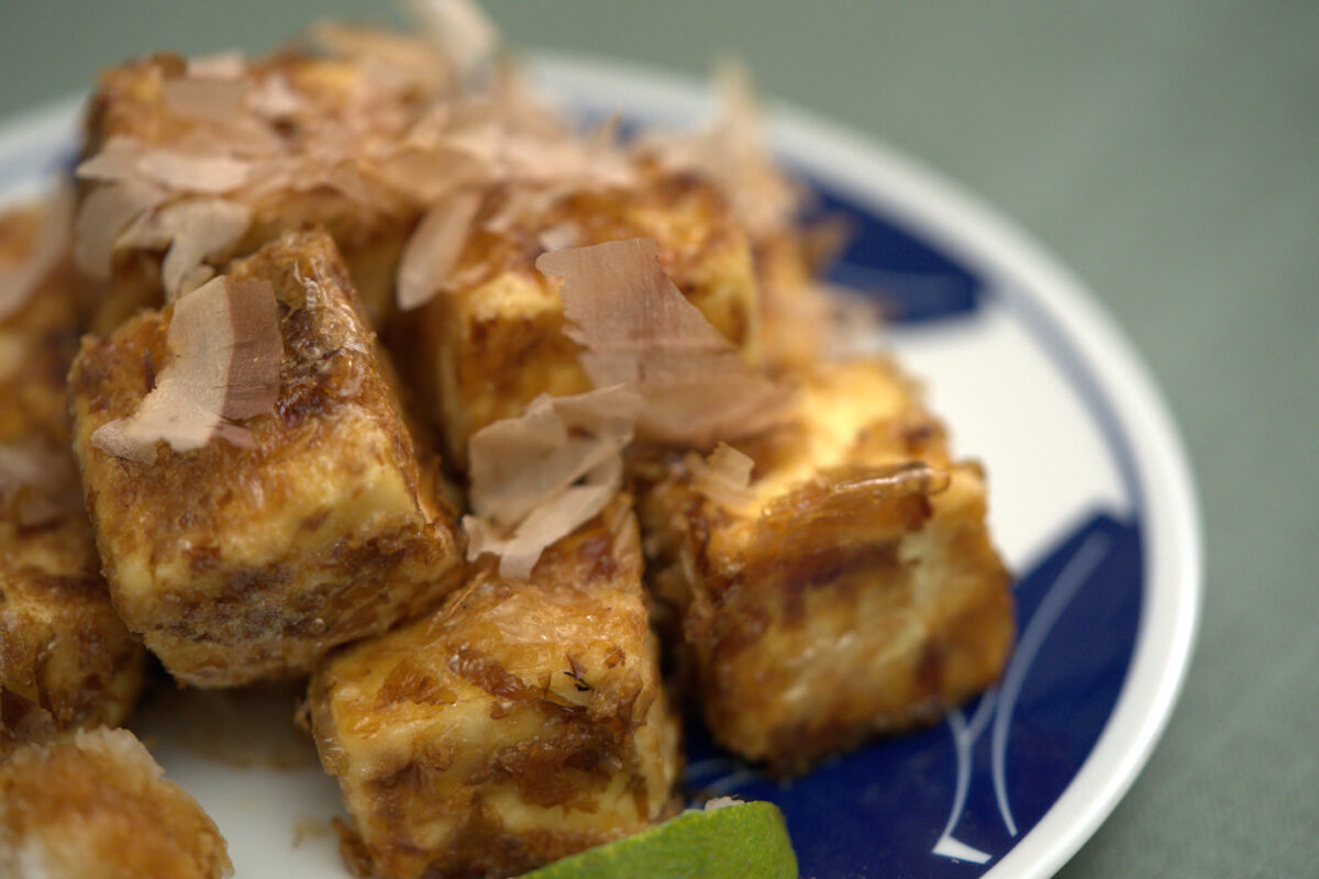 Cubed tamagoyaki (Japanese rolled omelette) pieces topped with katsuobushi (bonito flakes) served on a blue-and-white ceramic plate