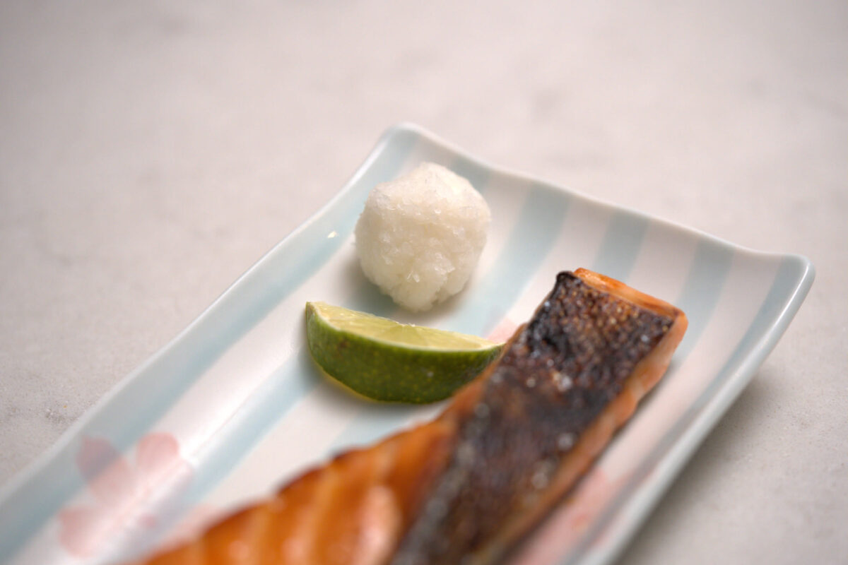 Grilled salmon fillet on a blue and white Japanese ceramic plate with a green citrus wedge (sudachi or lime) and a mound of grated daikon radish