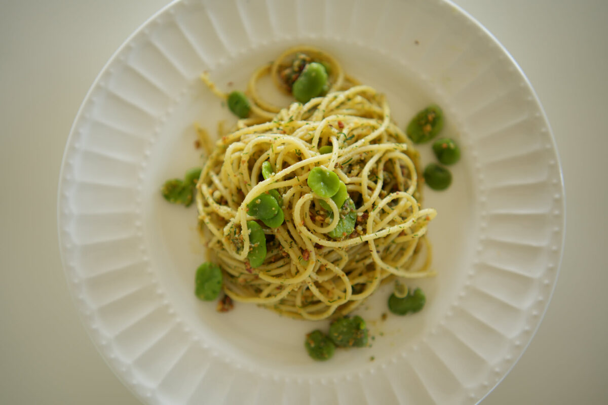 Overhead shot of spaghetti tossed in a herb and chili flake sauce, garnished with fresh green leaves and small round green beans, served on a white ribbed plate
